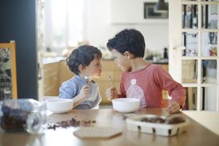 Irmãos se encarando na mesa enquanto comem café da manhã