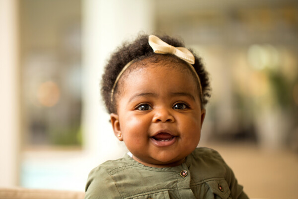 Bebê negra com lacinho amarelo na cabeça, sorrindo para a câmera
