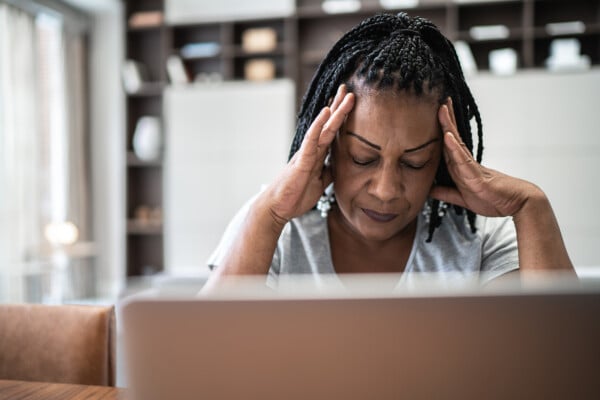 Mulher negra com as mãos na cabeça, cansada mentalmente, em frente a um laptop.