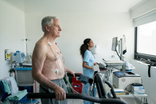 Homem idoso em uma esteira, fazendo um teste de stress no hospital enquanto enfermeira olha para o monitor cardíaco