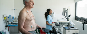 Homem idoso em uma esteira, fazendo um teste de stress no hospital enquanto enfermeira olha para o monitor cardíaco