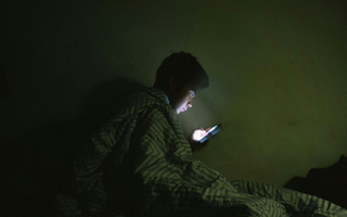 Jovem utilizando o celular no escuro do seu quarto