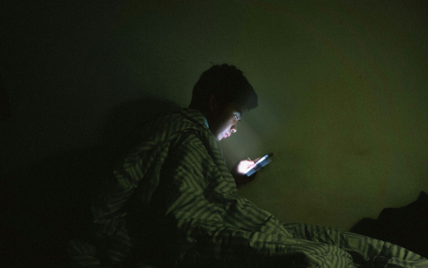 Jovem utilizando o celular no escuro do seu quarto