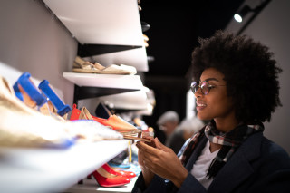 Mulher jovem de pele negra e cabelos crespos olhando uma prateleira de sapatos em uma loja