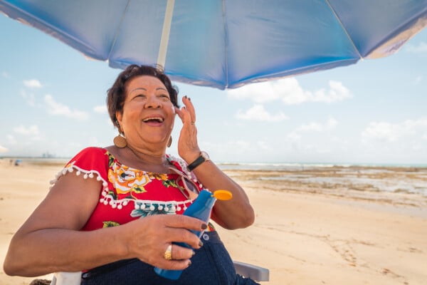 Mulher passando protetor solar embaixo de guarda-sol na praia