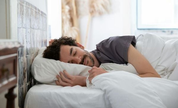 Homem branco sorrindo dormindo em uma cama