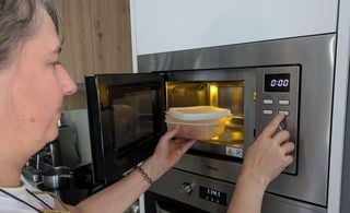 Mulher aquecendo alimento no microondas