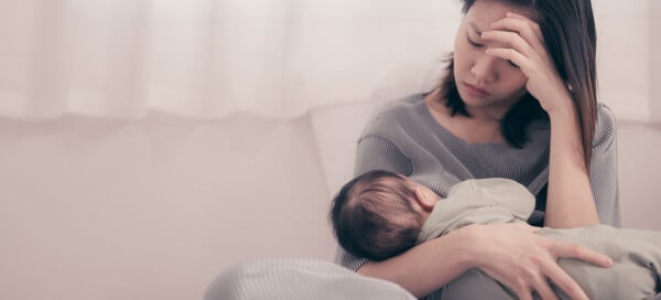 Mulher asiática com expressão séria segura um bebê recém-nascido no colo