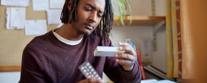 Homem lendo a embalagem de um remédio em comprimido