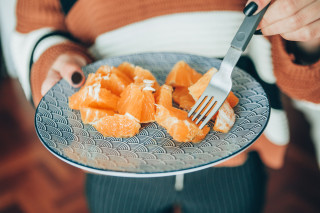 Mulher com prato de laranja e garfo na mão