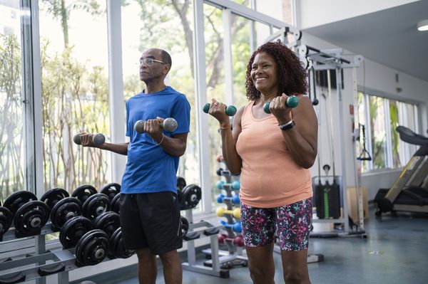 Homem e mulher fazendo exercício com halteres em academia de ginástica