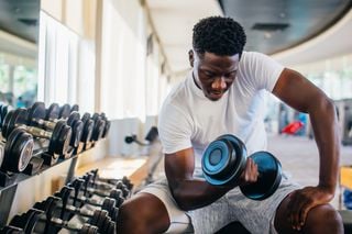 Homem negro fazendo exercício de musculação com halter na academia