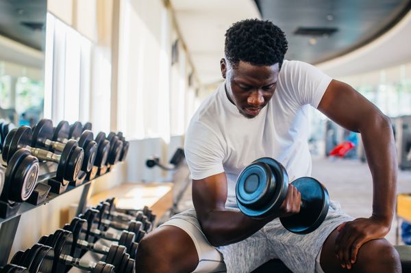 Homem negro fazendo exercício de musculação com halter na academia