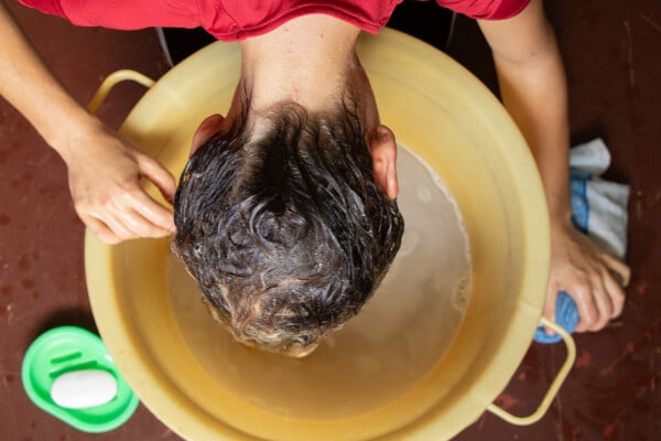 Na imagem, uma mulher de cabelos molhados está em frente a uma bacia realizando a técnica squish to condish