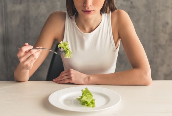 Mulher sentada a mesa comendo uma folha de alface que está em um prato