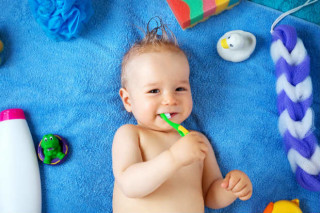 Bebê segurando uma escova de dentes enquanto está deitado em cima de uma toalha - Foto: Getty Images