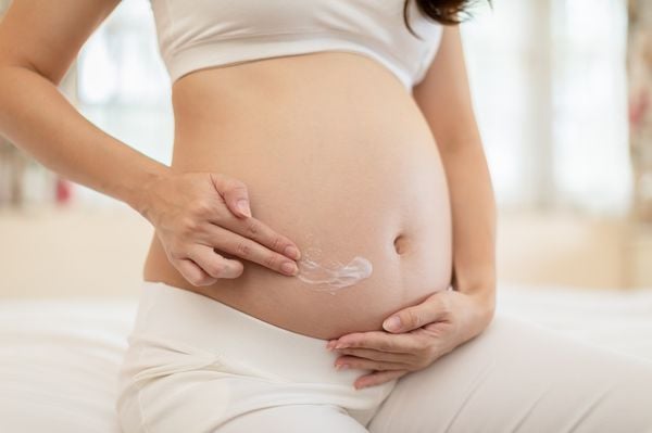 Mulher grávida passando um creme na barriga