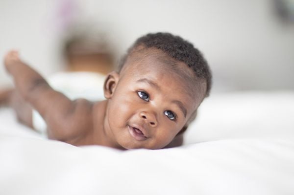 Bebê negro deitado na cama, com um sorriso no rosto