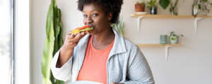 Mulher comendo um pão com folhas verdes e tomates enquanto segura um prato