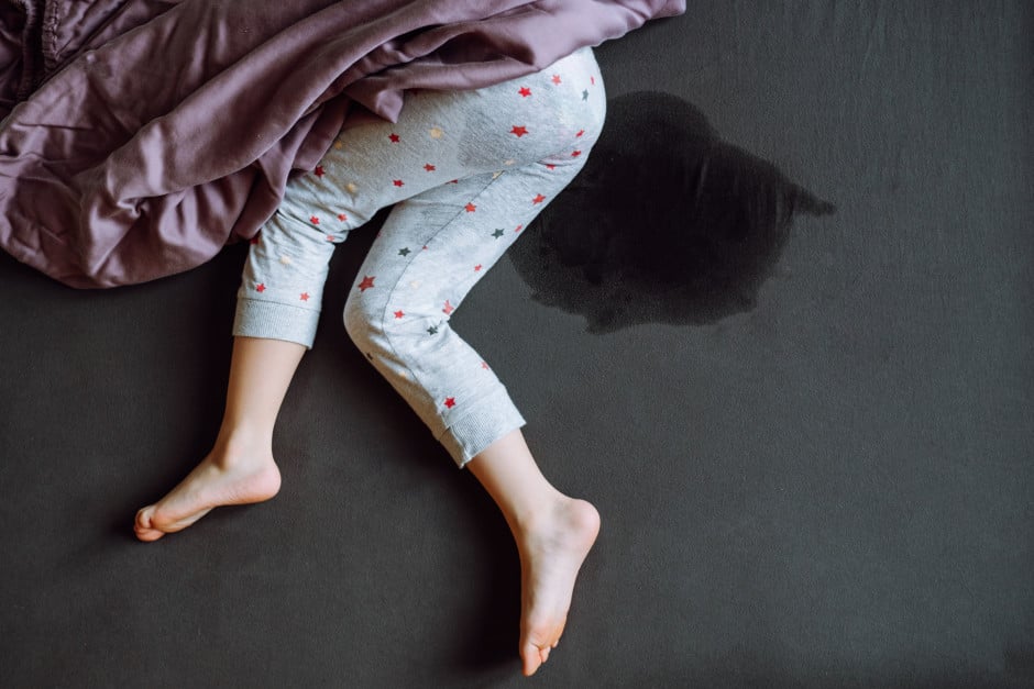 Imagem mostrando criança fazendo xixi na cama enquanto dorme, sem mostrar o rosto.