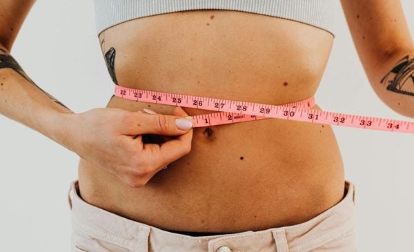 Close up da barriga de uma mulher que tira suas medidas com uma fita