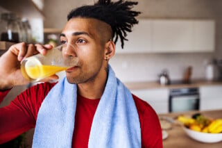Homem com toalha ao redor do pescoço bebendo um suco de laranja