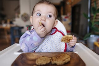 Bebê sentada em cadeirinha comendo biscoitos