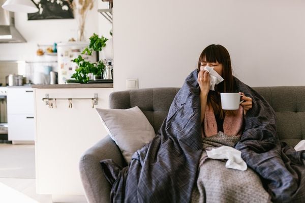 Mulher gripada sentada em um sofá tomando chá