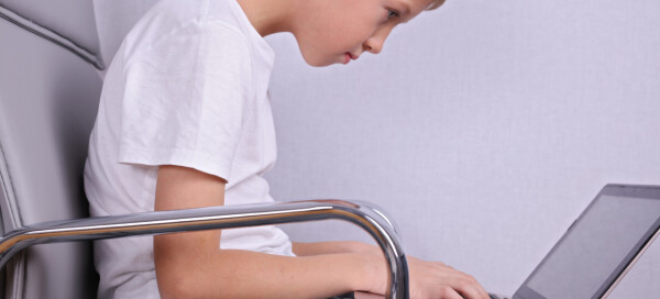 Garoto adolescente sentado em uma postura ruim em uma cadeira, com um notebook no colo