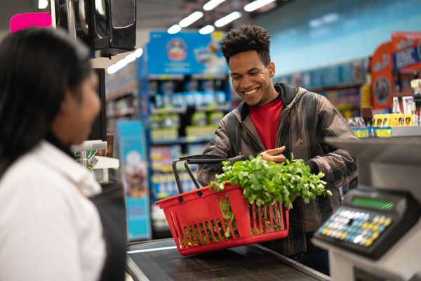 Homem jovem comprando vegetais em caixa de supermercado