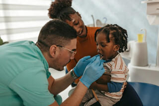 Dentista examinando os dentes de uma criança com um equipamento dentário. A criança está sentada no colo da mãe