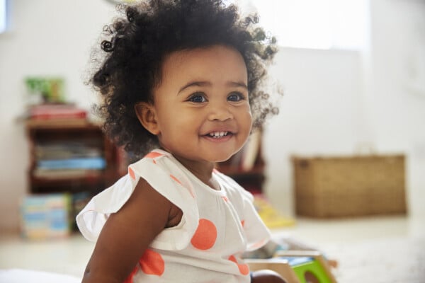 Menina pequena, bebê, sorrindo sentada na sala, ao redor de brinquedos