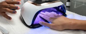 mão de uma mulher dentro de uma câmara de luz UV para secar as unhas de gel