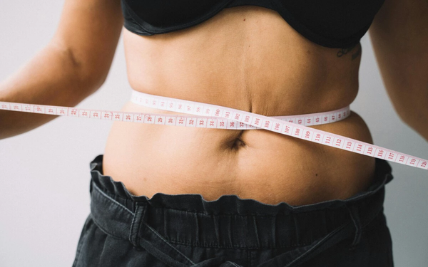 Mulher medindo a própria barriga com fita métrica
