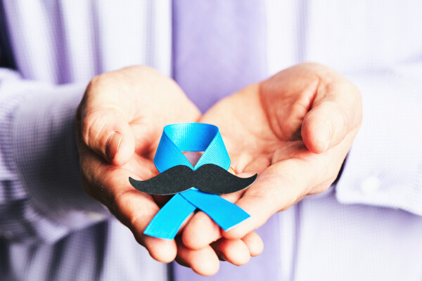 Mãos masculinas segurando uma fita azul com bigode que representa o movimento de consciência sobre o câncer de próstata, Novembro Azul
