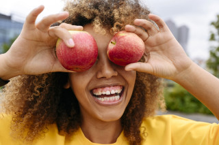 mulher sorrindo, segurando duas maçãs na altura dos olhos