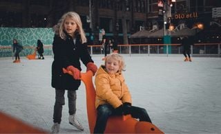 Duas crianças brincando em uma pista de patinação no gelo