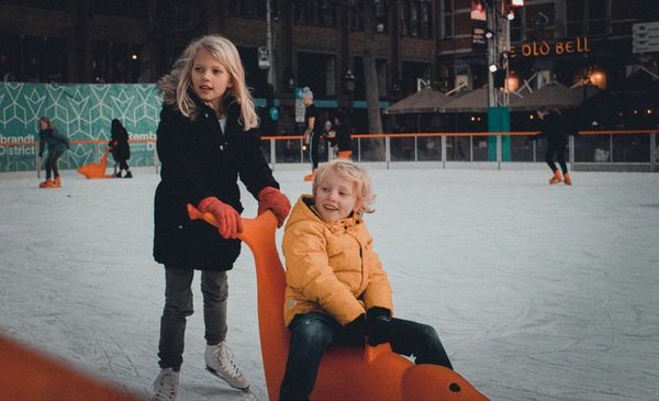 Duas crianças brincando em uma pista de patinação no gelo