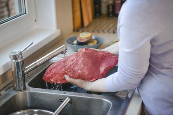 Mulher lavando uma peça de carne bovina na pia da cozinha