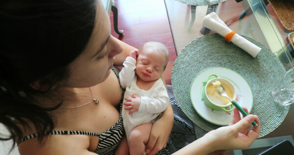 Mãe comendo enquanto bebê recém nascido dorme
