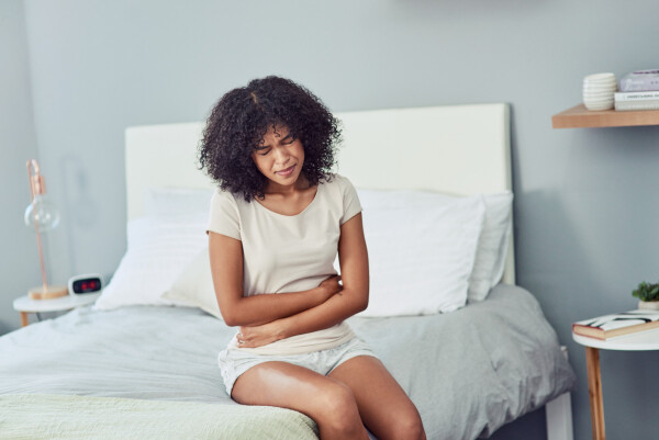 Mulher jovem negra sentada em sua cama com dores abdominais