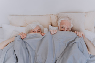 casal idoso deitado na cama se cobrindo com um cobertor