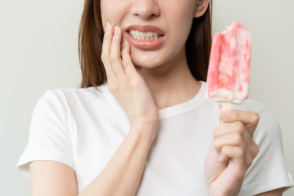 Mulher segurando picolé, com expressão de dor por sensibilidade nos dentes