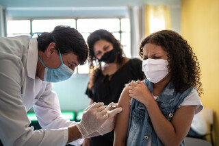 Criança sendo vacinada por médico. Uma mulher está atrás da criança