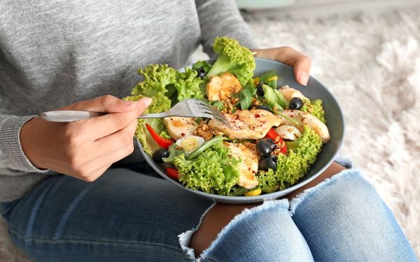 pessoa comendo um prato de salada com filé de frango