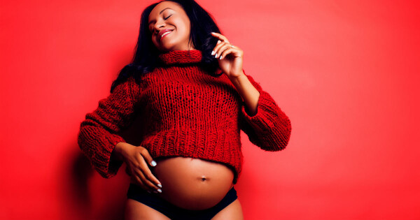 Mulher grávida sorrindo em frente a um fundo vermelho