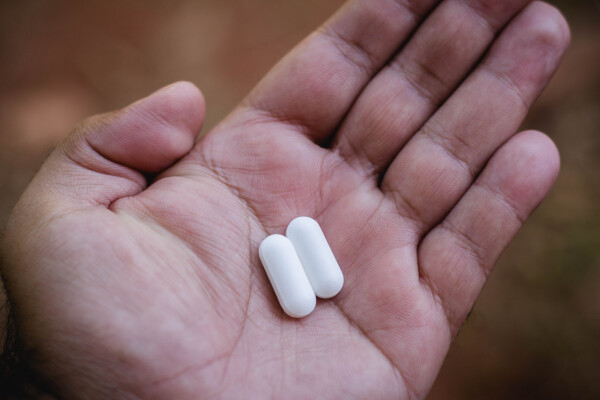 Foto aproximada de duas pílulas brancas na mão de um homem.