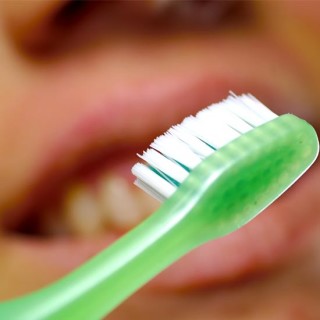 Pessoa escovando os dentes com uma escova verde