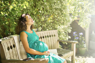 Mulher grávida sentanda em banco no sol
