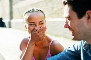 Mulher negra escondendo a boca rindo enquanto olha para um homem